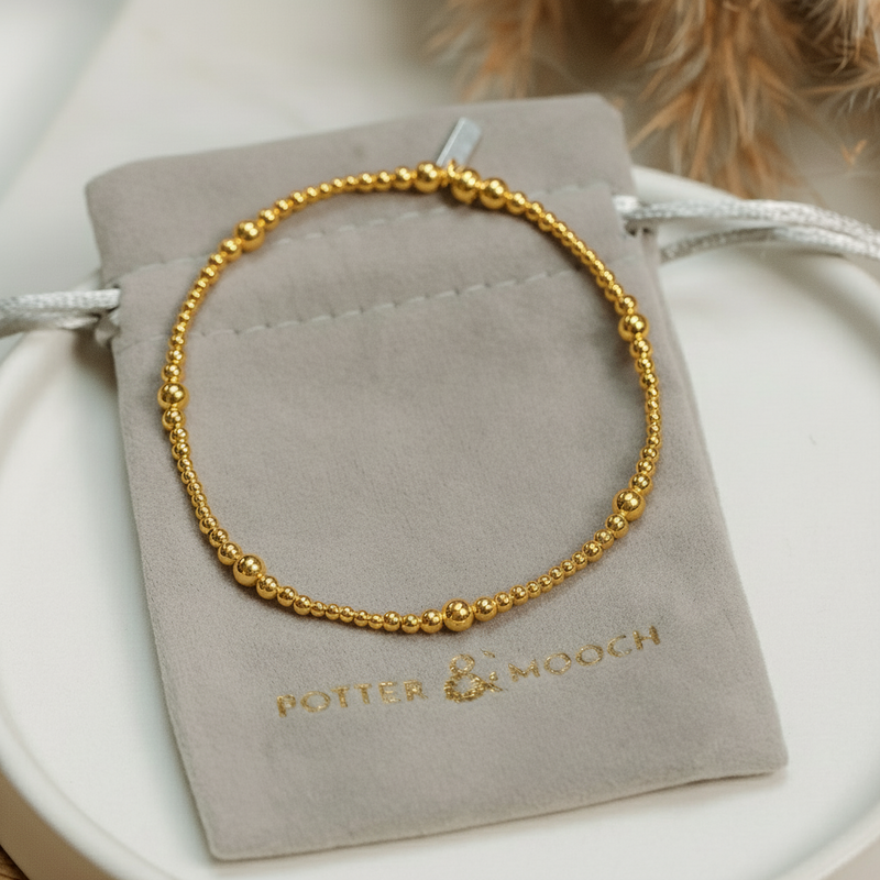 gold  bracelet on a Potter & Mooch branded grey pouch with a blurred natural background