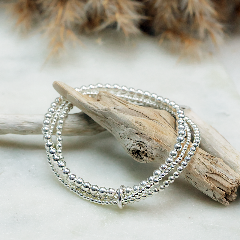 Silver bracelets on a piece of driftwood with a natural background