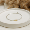 Silver bracelet with gold accents on a white plate, with a blurred brown animal in the background.