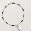 Bracelet with green beads and a tree charm on a white plate