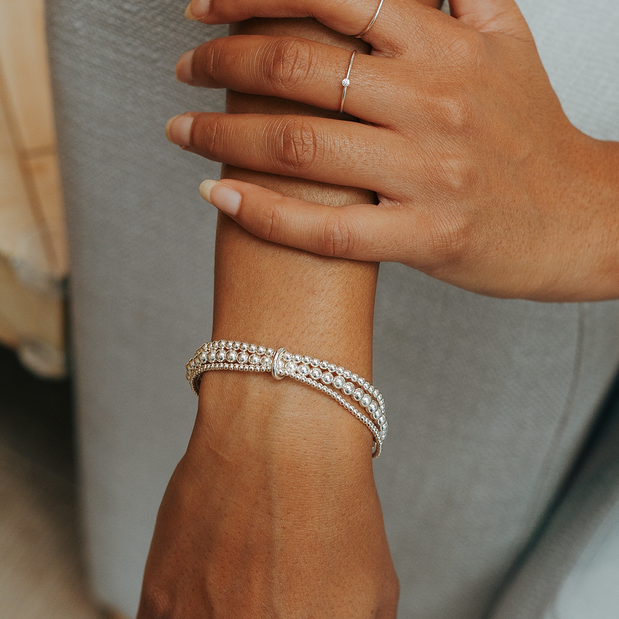 Close-up of a person's arm wearing two silver bracelets on a blurred background