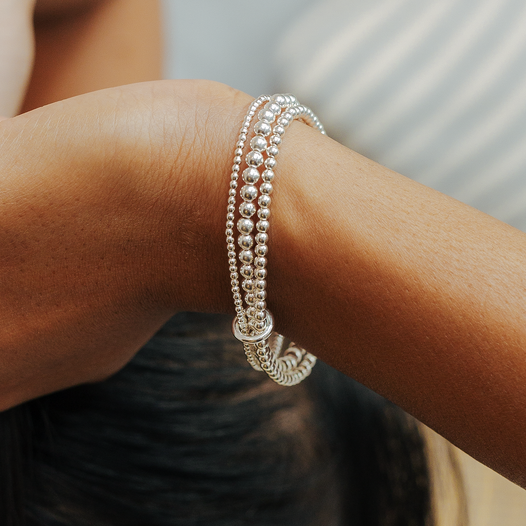 Close-up of a person's arm wearing two silver bracelets on a blurred background