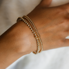 Gold bracelets on a wrist with a neutral background