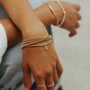 Close-up of a person's wrist with multiple gold bracelets on a neutral background