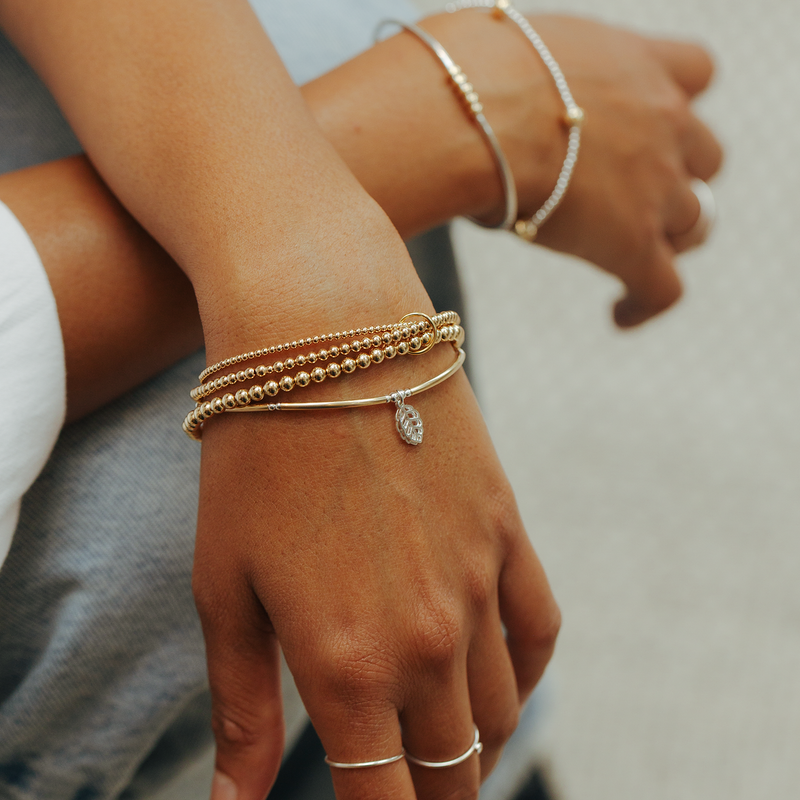 Close-up of a person's wrist with multiple gold bracelets on a neutral background