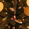 Decorative ornament of Santa Claus on a snowboard with a gift, hanging against a plain background.